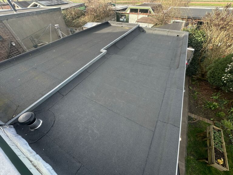 Plat dak met ventilatie en tuin op achtergrond.