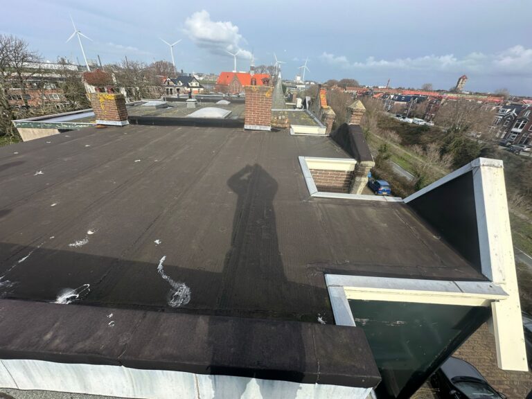 Plat dak met schoorstenen en windmolens op achtergrond.