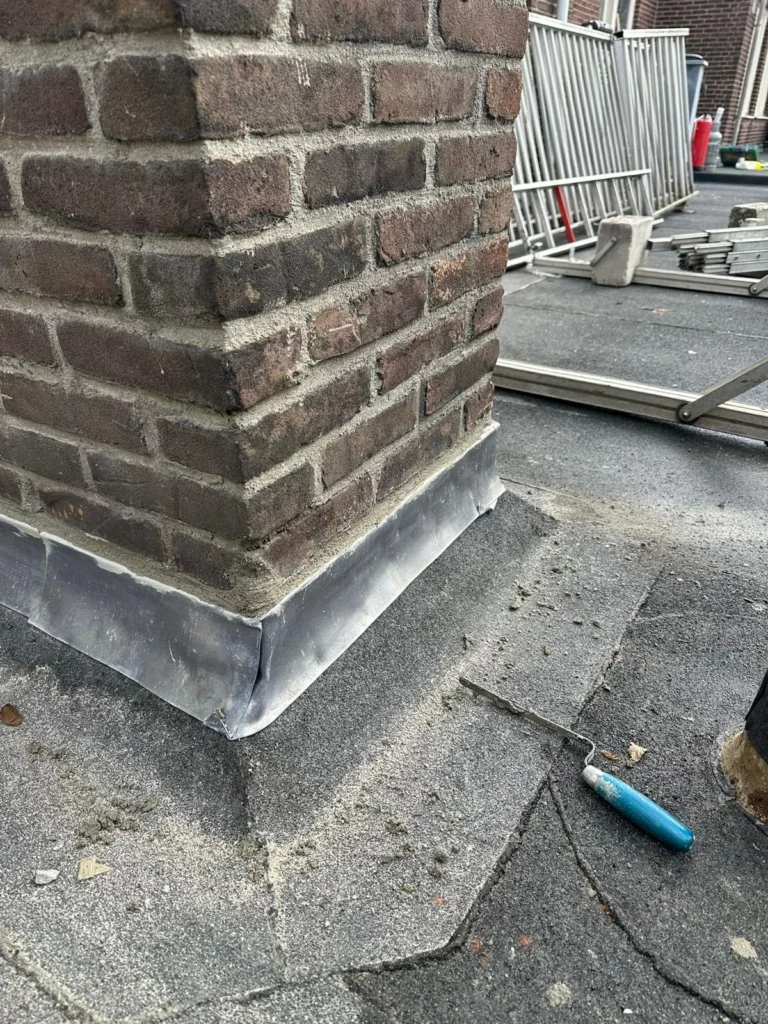 Schoorsteen op een plat dak met nieuwe loodaansluiting rondom in Westzaan